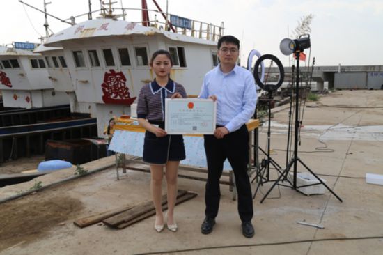 海鮮電商張夢琴與幫辦員手持食品經營許可證合影。贛榆區(qū)委宣傳部供圖