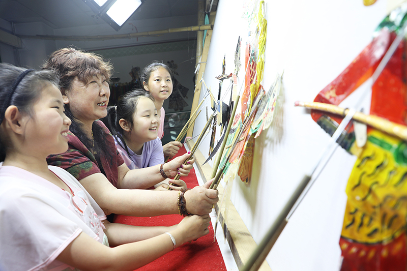 皮影藝人指導(dǎo)小朋友表演皮影戲。