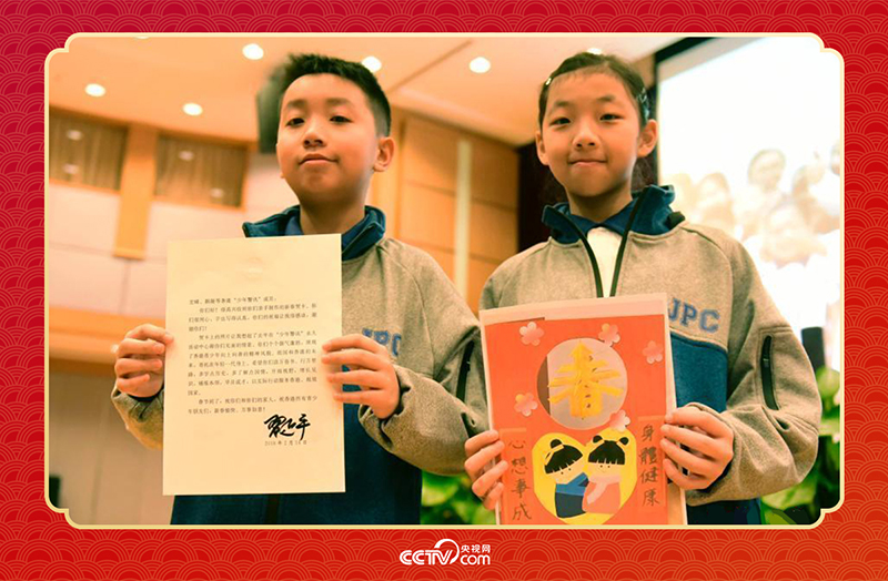 圖為香港“少年警訊”成員郭宏晞（左）展示習(xí)主席回信、羅顥凝（右）展示送給習(xí)主席的賀卡并合影。